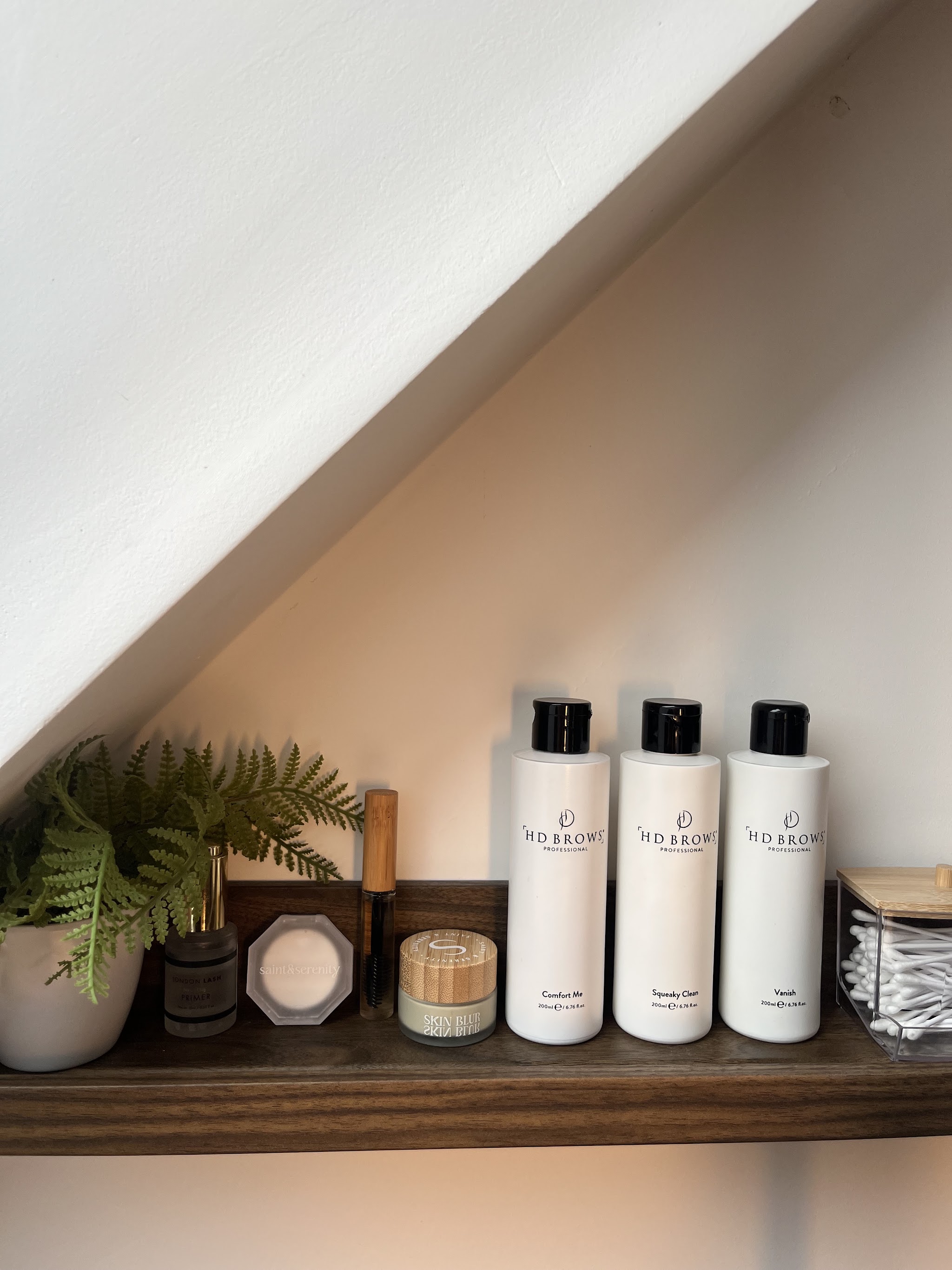 Shelf of lash products and a plant under the sloped ceiling